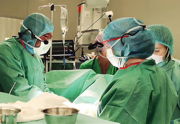 Surgical team performing operation in sterile operating room with instruments, monitors, and emergency equipment.